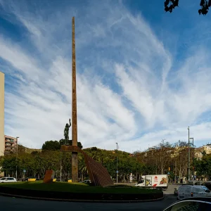 Desnuda y altiva, una mujer joven levanta el brazo sosteniendo una rama de laurel en la mano, símbolo de libertad y futuro. Es Flama, una estatua de bronce de 4,5 metros, creada por el escultor Josep Viladomat en 1934 e instalada en el enorme monolito que preside la plaza de Llucmajor, en el cruce del paseo de Valldaura con el de Verdum y Via Júlia. Flama, estatua y medallón se inauguraron en 1936 en el centro de Barcelona, aunque su historia venía de años antes.