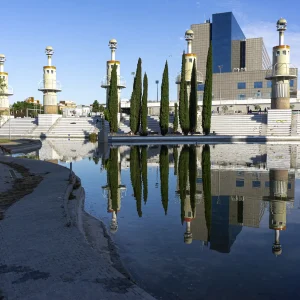 De esta plaza, destaca la poderosa presencia de nueve torres faro. Aquí, los peldaños, cubiertos de baldosa blanca, permiten sentarse o bajar hasta las isletas con bancos que se adentran en el lago. La otra pendiente con peldaños discurre paralela al pasaje que comunica la entrada principal del parque con el otro extremo. La antigua industria que da nombre al parque era una empresa textil fundada por la familia Muntadas en 1847.