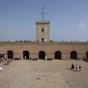 En el piso superior del patio de armas, en la fachada delantera, se conserva una torre de vigía cuadrada, totalmente remodelada. Se trata de un lejano testimonio del faro o atalaya de vigilancia, el precedente más antiguo del Castillo actual. La mención más antigua que se conoce data de 1073, y en ella se explicaba que durante el día el vigía avisaba de la presencia de naves hostiles con señales de velas, y de noche con señales de fuego. Desde el punto de vista de la estructura, la torre de vigía se transformó a base de sucesivas obras de remodelación entre los siglos XIV y XVII. Torre de vigilancia del Castillo de Montjuïc