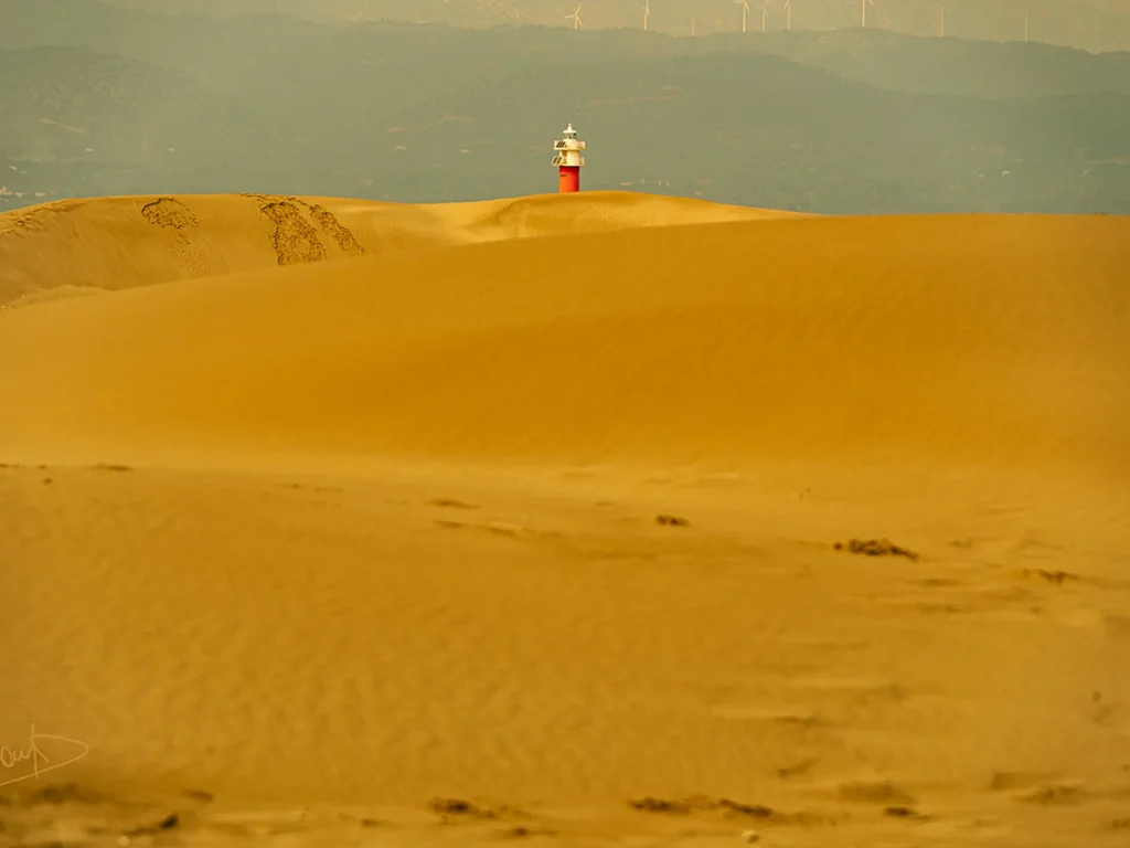 Entrelas dunas de la la playa del Fangar, se puede ver la óptica del faro que le da nombre a la playa. El Faro del Fangar sobresaliendo sobre las dunas