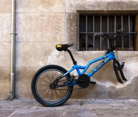 A veces no sabemos si algo espera o ya ha sido dejado atrás. Bicicleta incompleta atada a una ventana en un entorno urbano sucio y de apariencia abandonada.
